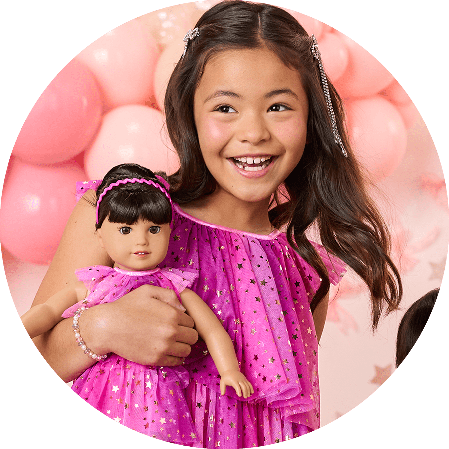 Young girl holding her doll in matching pink dress