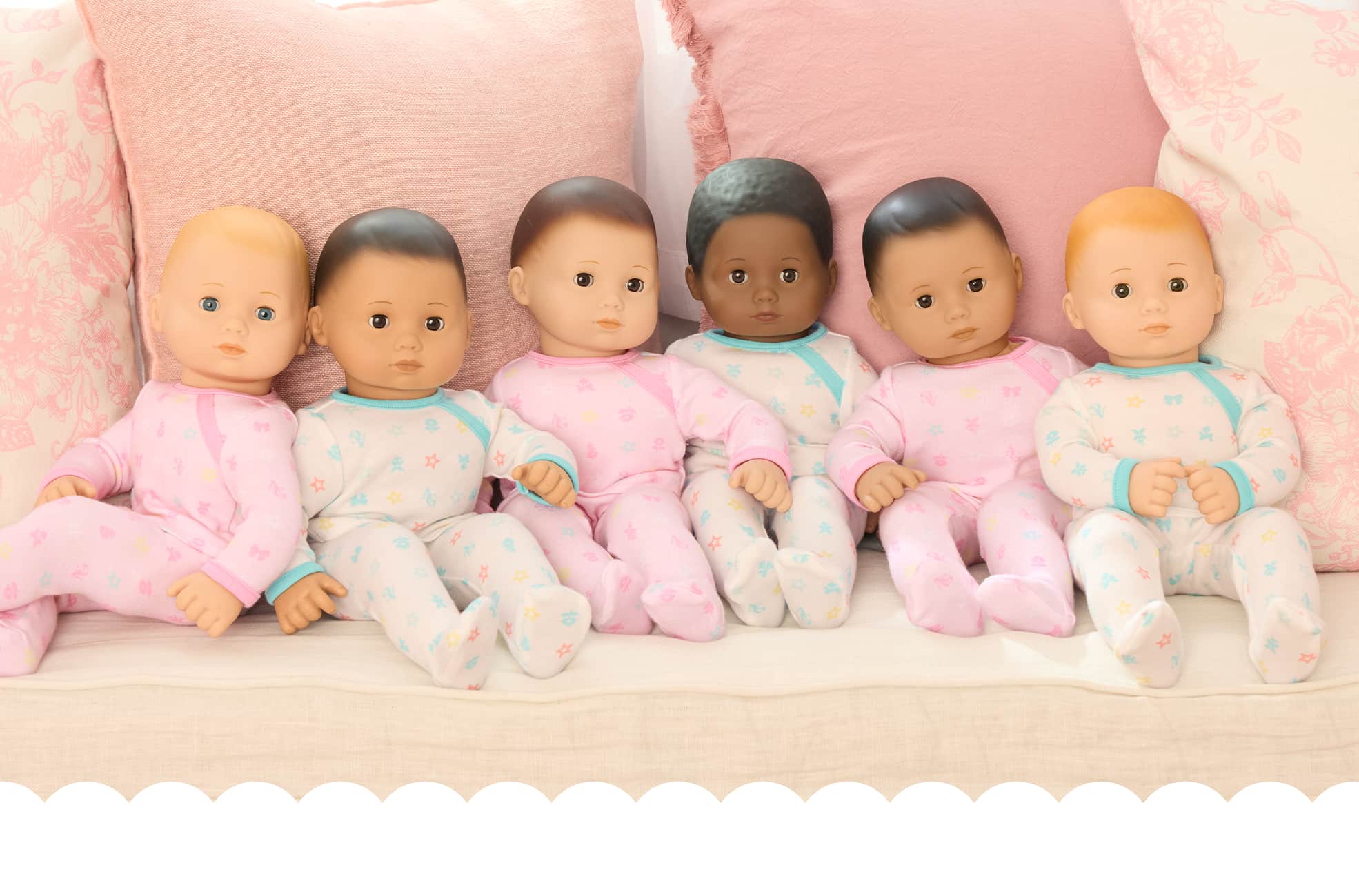 6 Bitty Baby dolls sitting up on a tan couch with pink pillows