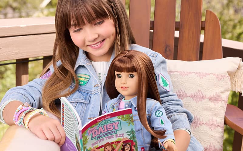 Girl sitting with Daisy Davenport doll reading Daisy Davenport Saves the Day book in matching jean jacket outfit