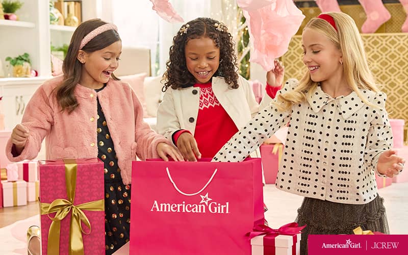 Three girls in J.Crew matching outfits opening an American Girl shopping bag